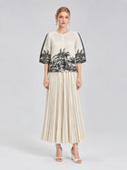 A woman stands against a plain light gray background wearing a cream top with black palm tree print and elbow-length sleeves, paired with Social Queen’s Striped Pleated Wide-Leg Pants and white heeled sandals.
