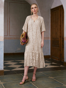 A woman stands indoors on a tiled floor, wearing the Social Queen Geometric Jacquard Mulberry Silk Dress, holding a colorful woven bag and gold heeled sandals.