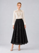 A woman models the Social Queen Floral Vine Embroidered Blouse, featuring delicate floral vine embroidery in ivory, paired with a long black lace skirt and silver heels. She showcases a relaxed straight silhouette against a plain light gray background.