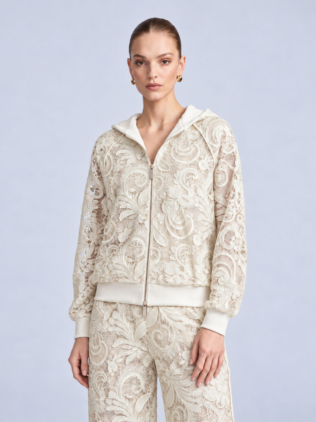 A woman wears a cream-colored, zip-up Paisley Embroidered Lace Hooded Jacket crafted from floral cutout lace.