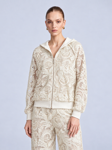 A woman wears a cream-colored, zip-up Paisley Embroidered Lace Hooded Jacket crafted from floral cutout lace.