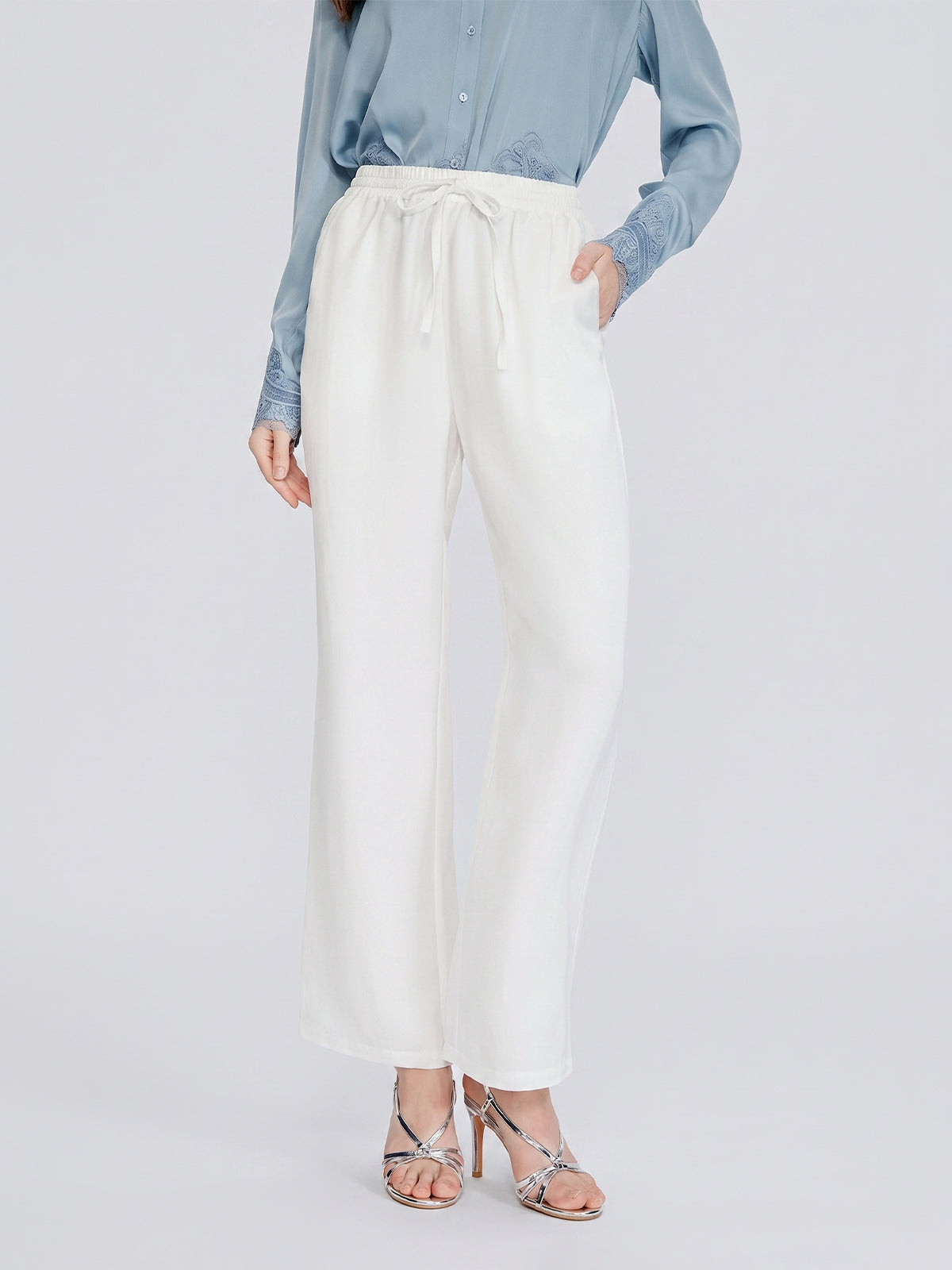 A person wearing a light blue blouse, silver strappy heels, and Social Queen Linen Straight-Leg Pants in white stands against a plain background.