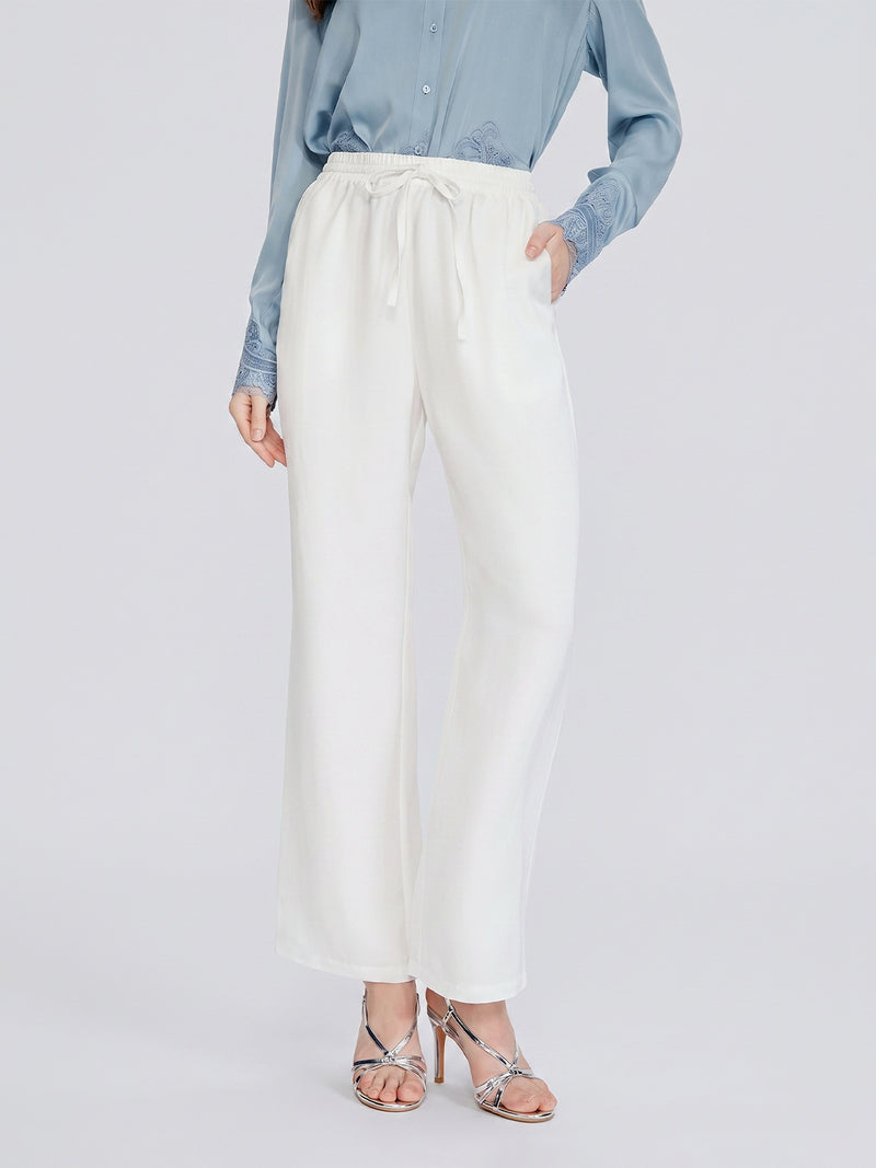 A person wearing a light blue blouse, silver strappy heels, and Social Queen Linen Straight-Leg Pants in white stands against a plain background.