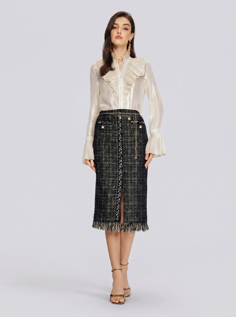 A woman stands facing forward against a plain light gray background, wearing a cream-colored ruffled blouse paired with the Social Queen Hand-Beaded Tweed Fringe Slit Skirt in black and gold, and beige heels.