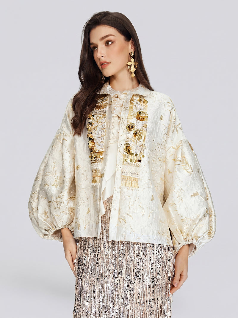 A woman models the Social Queen Beaded Jacquard Lantern Sleeve Jacket in cream, paired with a white blouse, gold earrings, and a silver fringe skirt, standing against a plain light background.