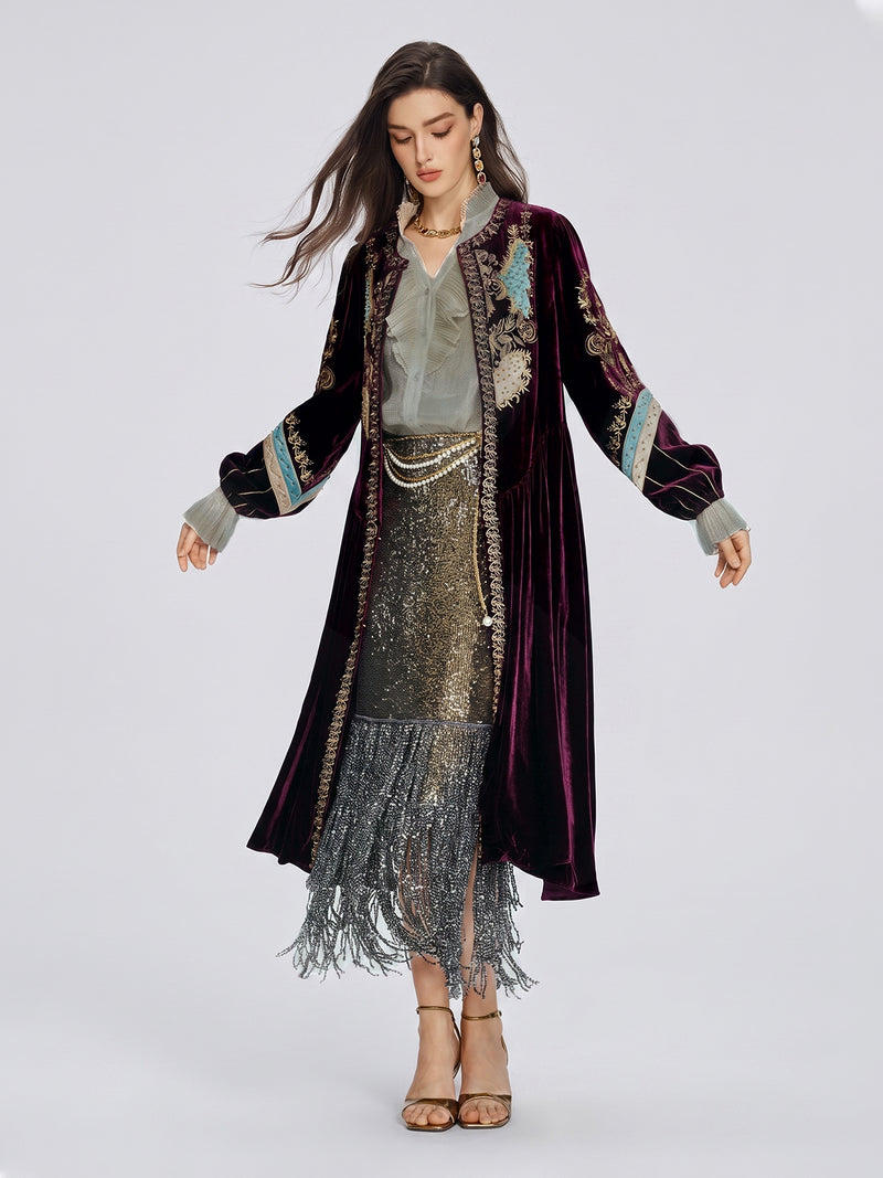 A woman wears the Handcrafted Embroidered Velvet Jacket by Social Queen over a beaded fringe dress, standing against a plain background.