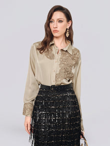 A woman wearing the Social Queen 100% Silk Retro Floral Appliqué Satin Blouse in beige, paired with a black sequined skirt with fringe and gold earrings, stands against a plain light background.
