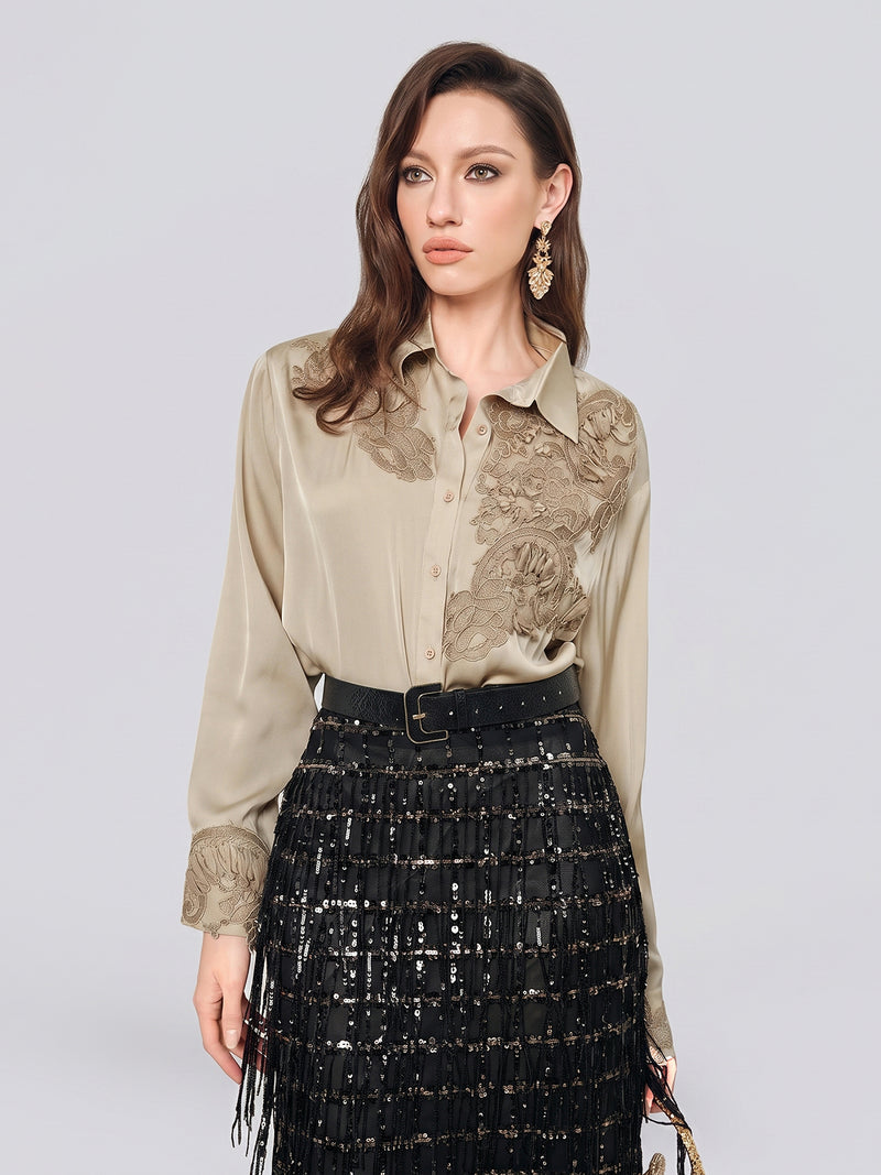 A woman wearing the Social Queen 100% Silk Retro Floral Appliqué Satin Blouse in beige, paired with a black sequined skirt with fringe and gold earrings, stands against a plain light background.