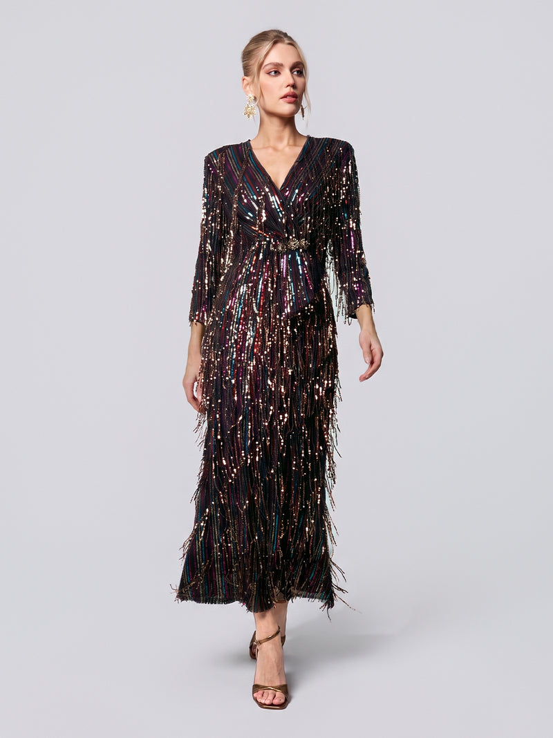 A woman models the Social Queen Sequin Fringe Slit Evening Gown—a black, sequin-embellished, long-sleeve formal dress featuring a deep V-neckline—paired with strappy high-heeled sandals as she walks against a plain light gray background.
