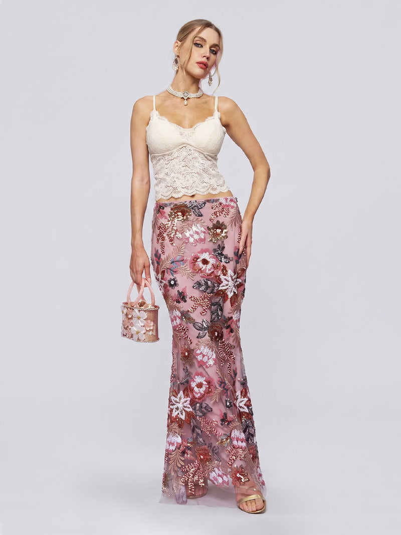 A woman poses against a plain light background wearing the Social Queen Floral Embroidered Sequin Mermaid Skirt, paired with a cream lace camisole and holding a small floral handbag.