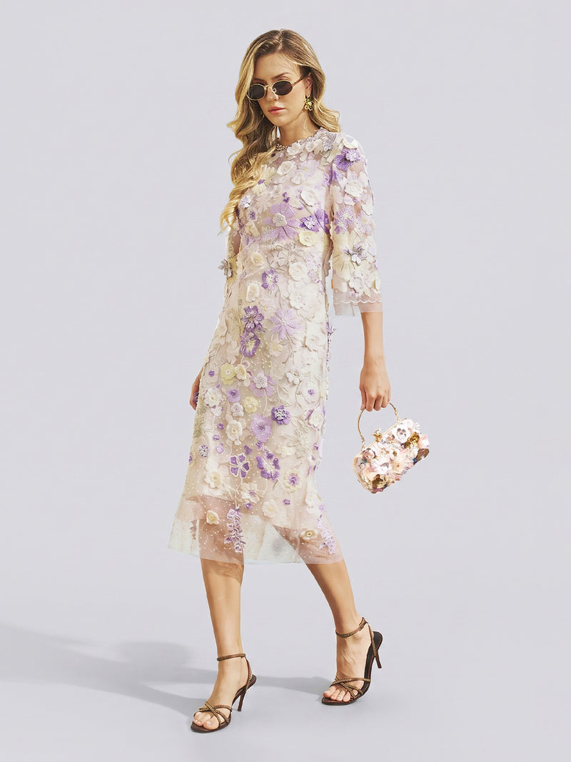 A woman in sunglasses wears the Social Queen 3D Floral Embroidered Beaded Dress—a sheer, knee-length design with purple and white floral appliqués and delicate beadwork—paired with a matching floral handbag and black strappy heels as she walks in front of a plain background. The dress’s subtle cheongsam-inspired silhouette offers an elegant, fashion-forward option for any stylish wedding guest.