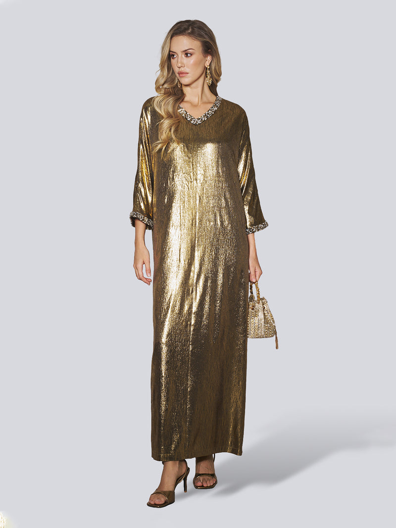 A woman wearing the Social Queen Metallic Crystal-Embellished Slit Dress, featuring three-quarter sleeves and a loose, shiny gold finish, styled with a small textured gold handbag and heeled sandals—an elegant choice ideal as a wedding guest dress.