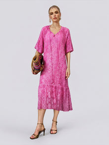 A woman stands against a plain light background wearing the Social Queen Geometric Jacquard Mulberry Silk Dress, holding a multicolored woven bag and gold heeled sandals.