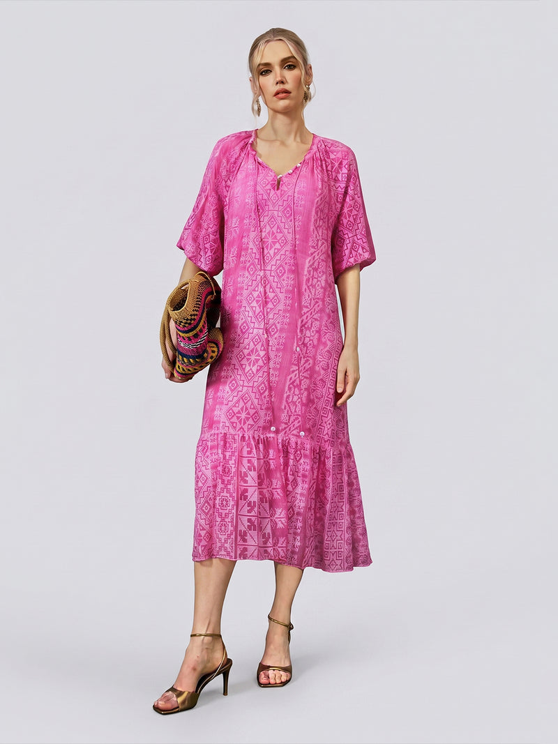 A woman stands against a plain light background wearing the Social Queen Geometric Jacquard Mulberry Silk Dress, holding a multicolored woven bag and gold heeled sandals.