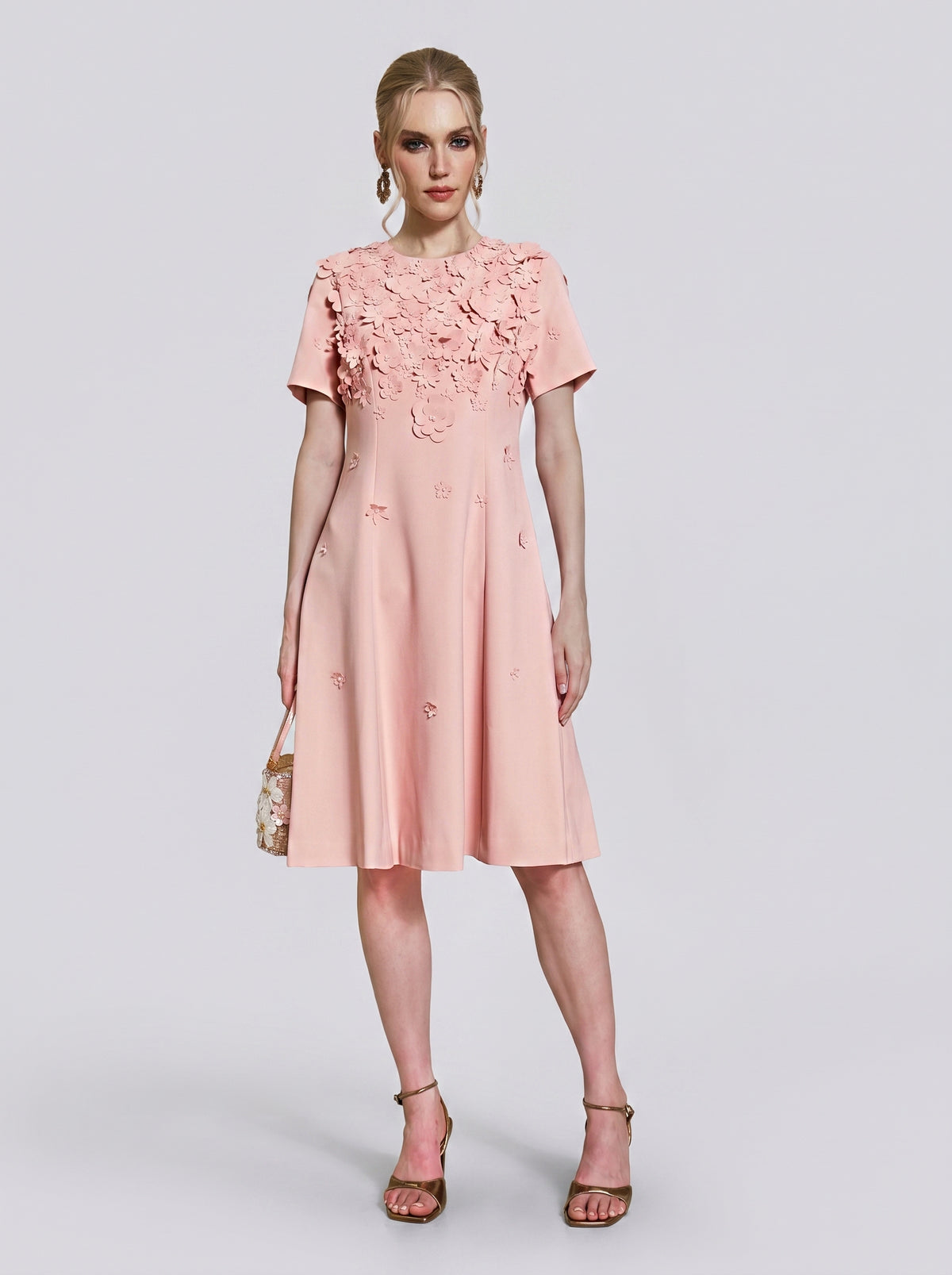 A woman models the Social Queen 3D Floral Appliqué A-Line Dress in light pink, featuring delicate 3D floral appliqués on the bodice and a knee-length A-line silhouette, while holding a small purse against a plain background.