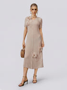 A woman stands against a plain light background wearing the Social Queen 3D Floral Pearl Embellished Pleated Dress in beige, styled with hoop earrings, heeled sandals, and a wooden handbag.
