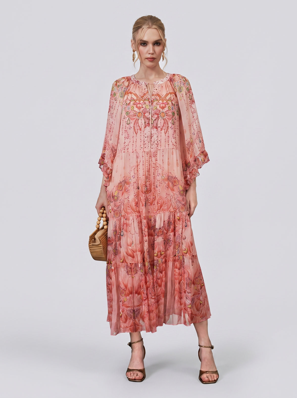 A woman stands against a plain light background, wearing the Social Queen Jewelry Print Mulberry Silk Dress—a resort-inspired maxi dress with sheer sleeves—paired with a wicker handbag and black strappy heels.