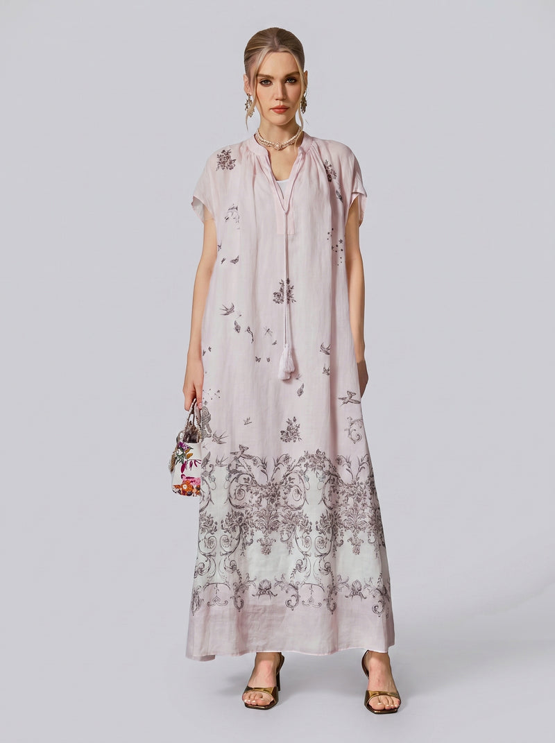 A woman wearing the Social Queen Baroque Garden Print Ramie Dress, a light pink maxi dress with vintage garden motifs and short sleeves (includes slip dress), stands against a plain background. Styled with a small handbag and heels, this effortlessly chic ensemble embodies elegant resort wear.