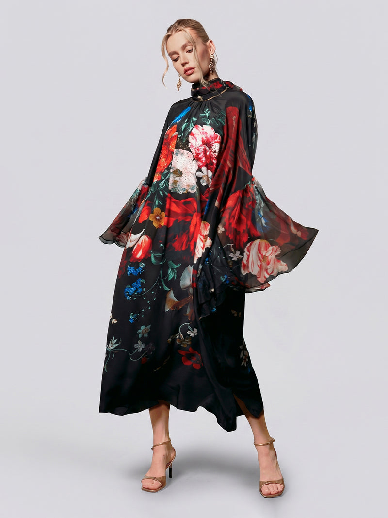 A woman wearing the Social Queen Artistic Floral Print Ruffle Dress, featuring large, colorful blooms and sheer, wide sleeves, stands in heels against a plain background.