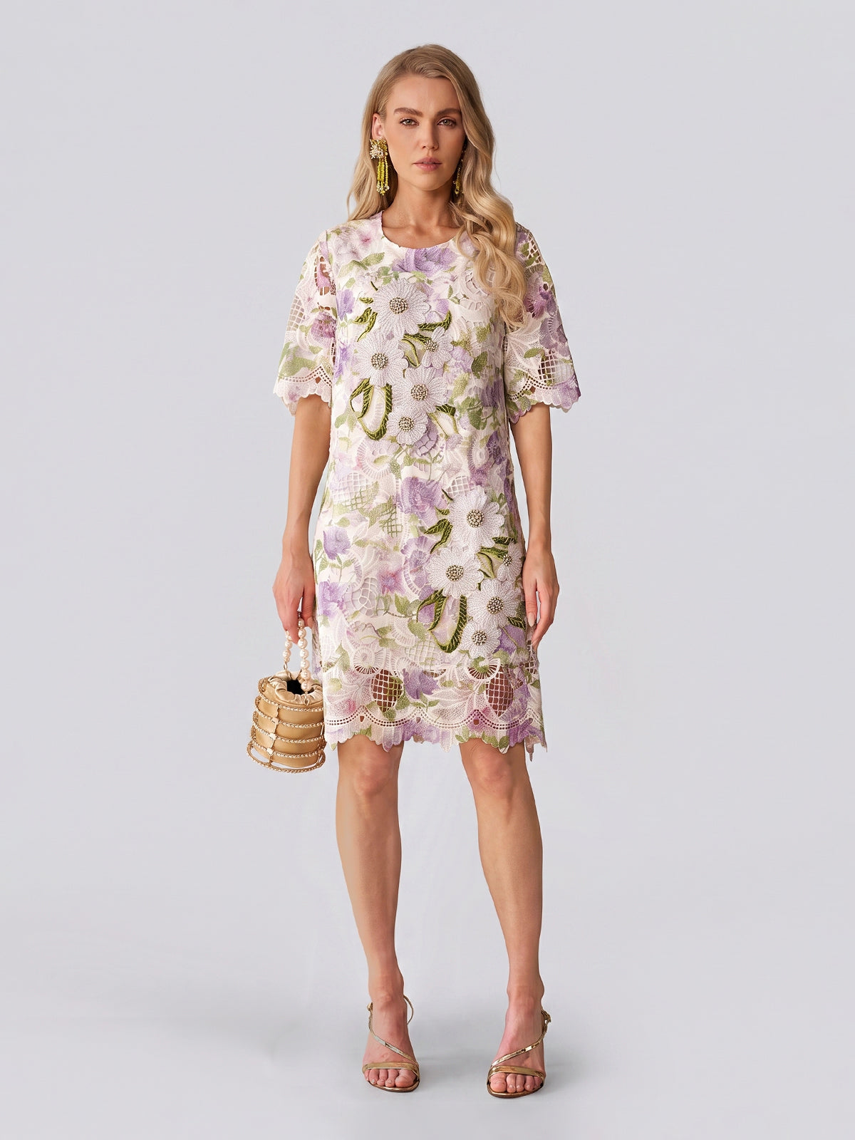 Dressed in the Social Queen Dimensional Embroidered Beaded Lace Dress, she stands against a light background, carrying a small woven handbag and wearing heeled sandals—a perfect look for a stylish wedding guest.