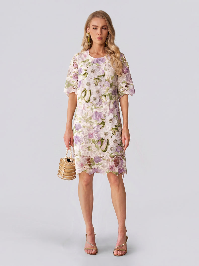 Dressed in the Social Queen Dimensional Embroidered Beaded Lace Dress, she stands against a light background, carrying a small woven handbag and wearing heeled sandals—a perfect look for a stylish wedding guest.