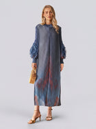 A woman stands against a plain light background wearing the Social Queen Gradient Pleated Dress with 3D Floral Sleeves, holding a bamboo handbag, styled with gold heels and drop earrings.
