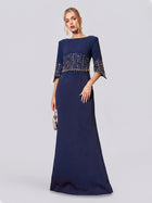 A woman stands against a plain, light background wearing the Social Queen Crystal Fringe Fishtail Gown—a floor-length, navy blue formal party dress featuring beaded embellishments on the bodice and sleeves—while holding a small handbag.