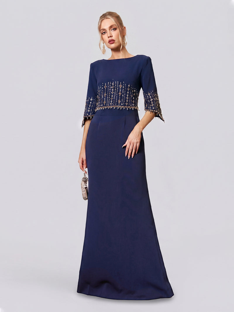 A woman stands against a plain, light background wearing the Social Queen Crystal Fringe Fishtail Gown—a floor-length, navy blue formal party dress featuring beaded embellishments on the bodice and sleeves—while holding a small handbag.