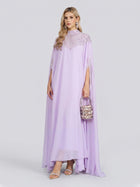 A woman wearing the Social Queen Beaded Tulle Caftan Cape Dress with delicate lace details stands against a plain background, holding a small handbag and wearing heeled sandals.