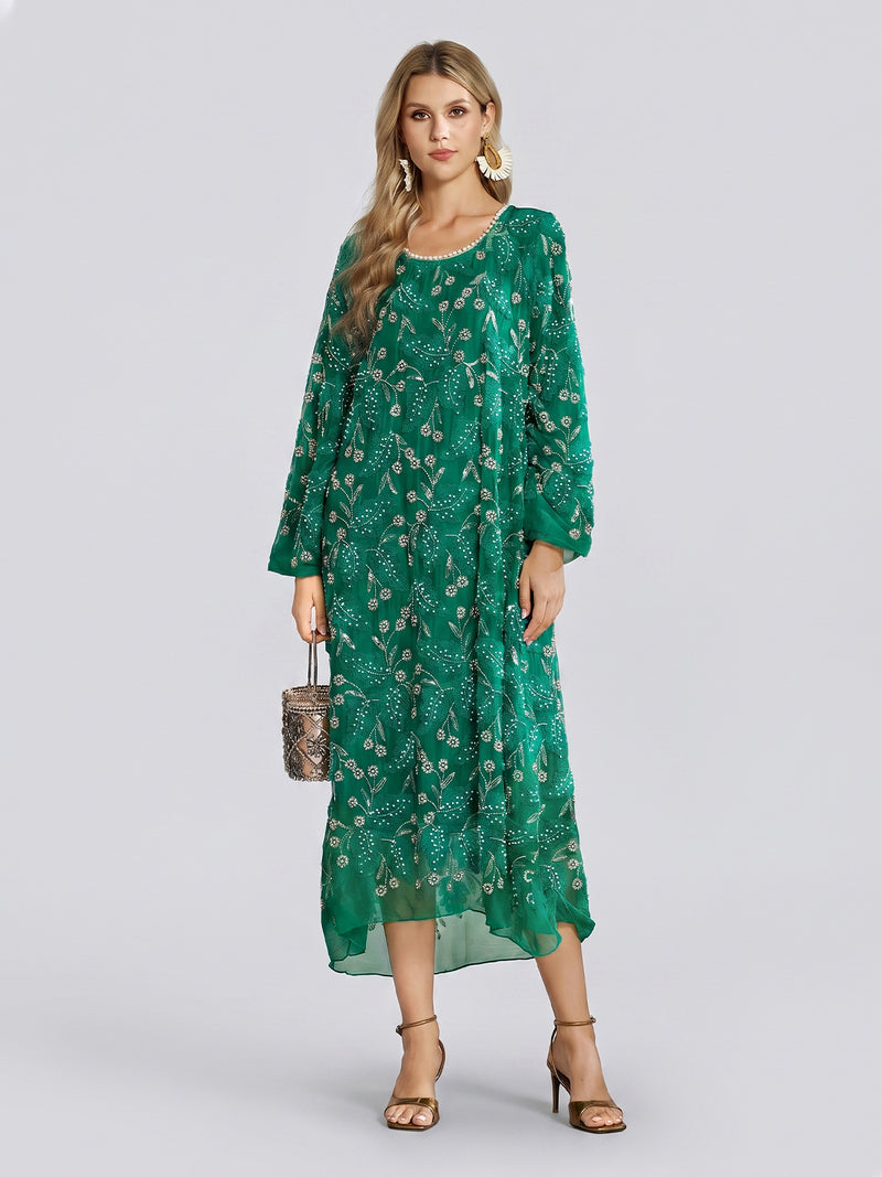A woman stands against a plain light background wearing the Social Queen 100% Silk Beaded Embroidery Dress—a loose-fitting, long-sleeve green silk tulle dress featuring gold patterns and delicate beaded floral embroidery—paired with gold earrings, gold heels, and a small metallic handbag.