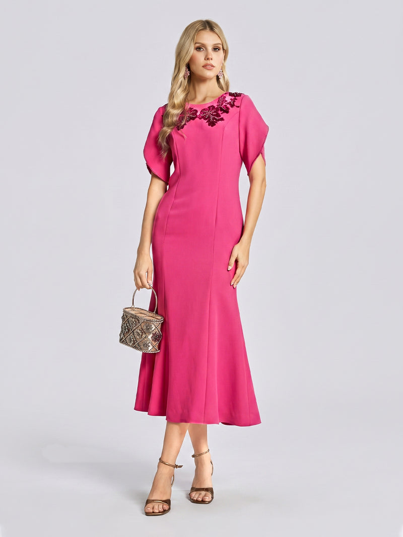 A woman poses against a plain background wearing the Social Queen Floral Embroidered Beaded Mermaid Dress—a vibrant rose-red gown with short sleeves and intricate 3D floral beading near the neckline. She completes the elegant special occasion look with heeled sandals and a small purse.