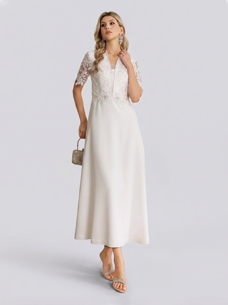 A woman models the Social Queen Lace-Panel Satin A-Line Gown—an elegant ivory dress featuring a graceful A-line silhouette and a delicate lace-paneled bodice. She accessorizes with a small handbag and stands against a plain light background.