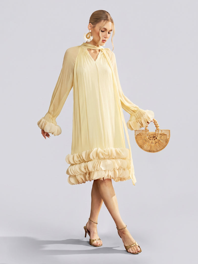 A woman stands against a plain light background, wearing the Social Queen Tiered Ruffle Silk Halter Dress in light yellow, styled with beige heels and a wooden handbag.