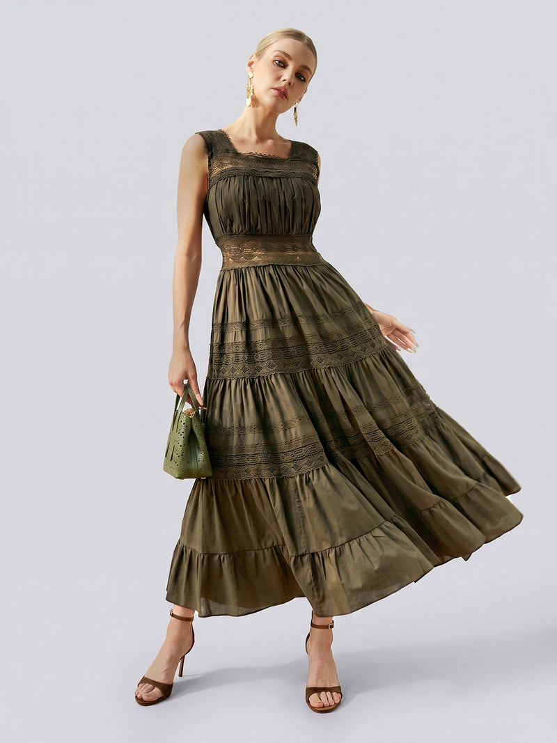 A woman poses against a plain light gray background, holding a small handbag and wearing the Social Queen Lace Detail Pleated Cotton Dress—an olive green, sleeveless maxi dress featuring lace detailing and a pleated tiered skirt.
