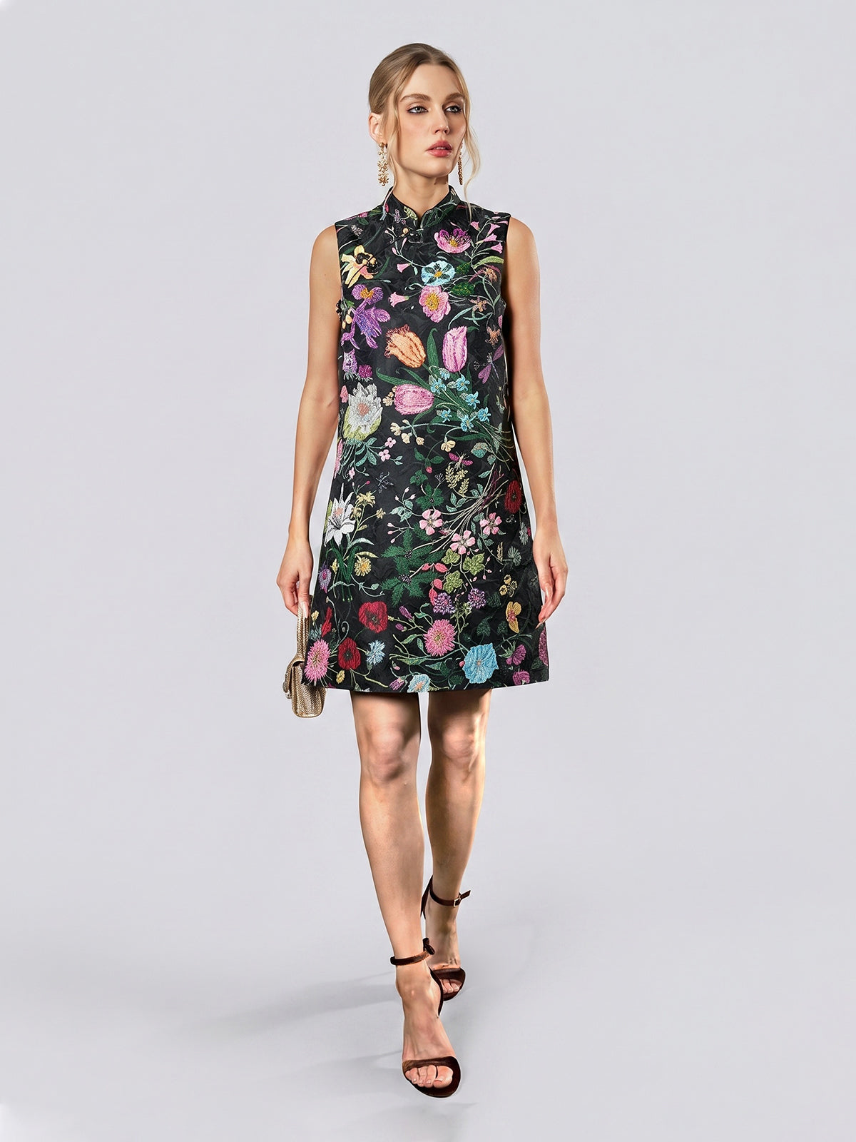 A woman dressed in the Social Queen Colorful Floral Mandarin Collar Dress—featuring a sleeveless silhouette, high neckline, and vibrant floral jacquard pattern—carries a small purse and walks in black heels against a plain light background.