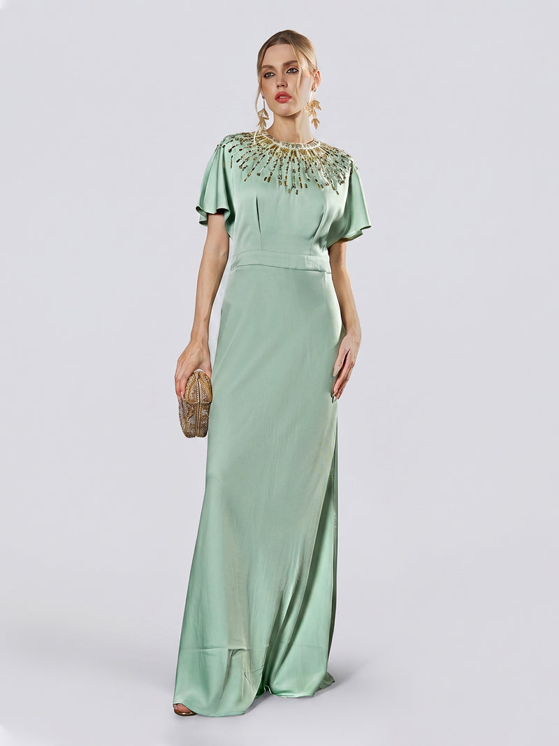 A woman wearing the Social Queen Beaded Satin Evening Gown in light green, featuring bead embellishments along the neckline, holds a small clutch while standing against a plain background.