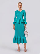 A woman stands against a plain background wearing the Social Queen Crystal-Embellished Pleated Peplum Set—a teal ensemble featuring a pleated peplum top and matching fishtail skirt. She accessorizes with a small handbag and silver sandals, making for a chic wedding guest look.
