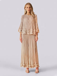 A woman stands against a plain light background, exuding effortless elegance in the Social Queen Layered Petal Beaded Pleated Set—a beige ensemble featuring a blouse with ruffled sleeves and beaded accents, paired with a matching long pleated skirt. This look is perfect for wedding guests.