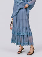 A person wearing the Social Queen Layered Lace Trim Skirt—a light blue, tiered chiffon design with floral lace trim and an A-line silhouette—paired with a matching top, brown high-heeled sandals, and carrying a small floral bag.