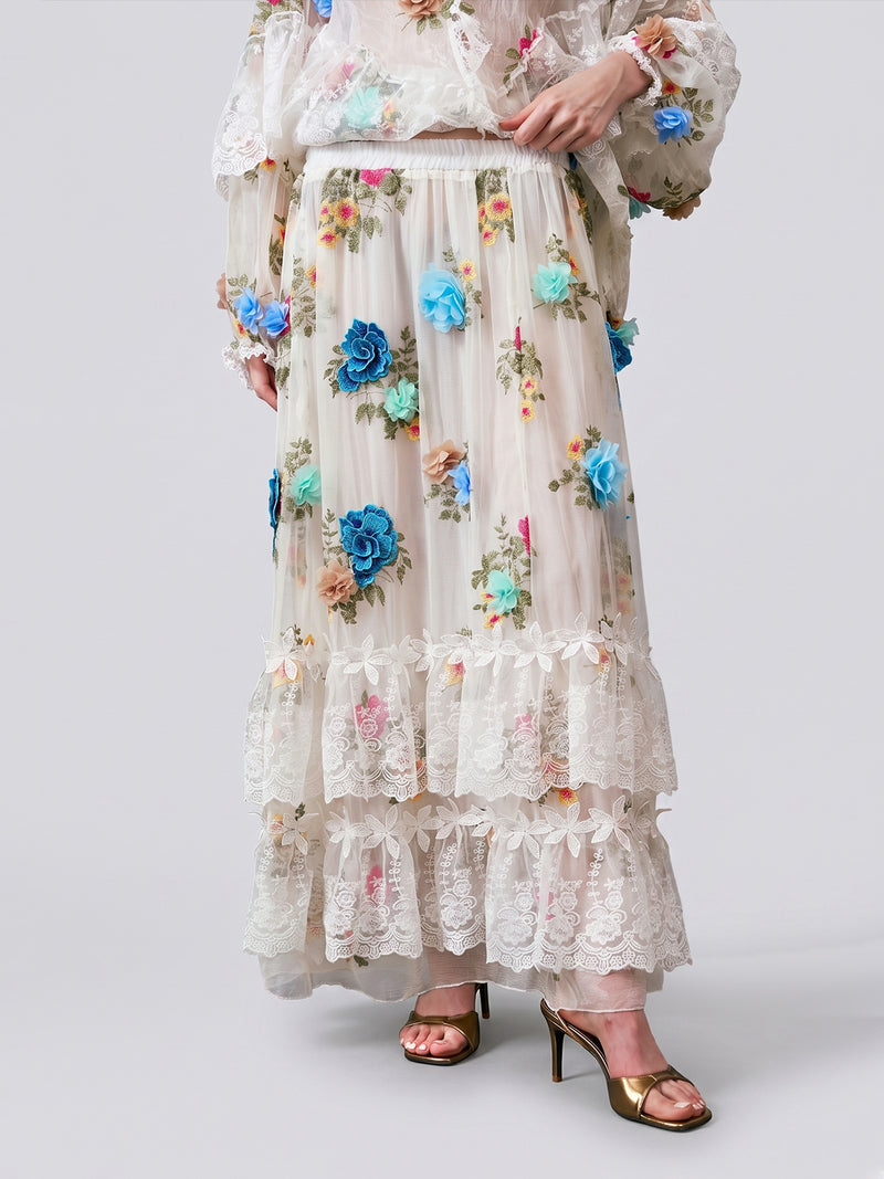 Wearing the Social Queen 3D Floral Appliqué Mulberry Silk Skirt—long, sheer cream silk adorned with floral embroidery and delicate lace ruffles—paired with a matching top featuring lace trim and gold open-toe heels. Only the outfit and lower body are visible.