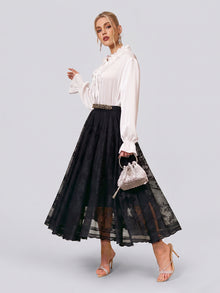 A woman in a white long-sleeve blouse and the Social Queen Jacquard Lace A-Line Midi Skirt, holding a small silver handbag and wearing strappy heels, stands against a plain light background. This elegant skirt features a high-waist A-line midi silhouette for timeless sophistication, making it an ideal choice for wedding guests.