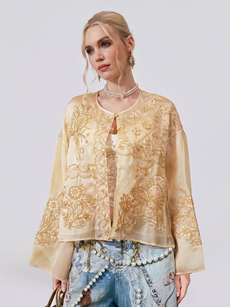 A woman wearing the Social Queen Ornate Bird Embroidered Silk Jacket over a lace top pairs it with blue pearl-embellished jeans, standing against a plain background.