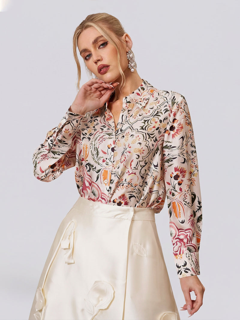 A woman models the Social Queen Artistic Floral Print Silk Blouse, featuring a relaxed tailored fit and long sleeves, tucked into a cream satin skirt with floral appliqué details, posed against a plain light background.