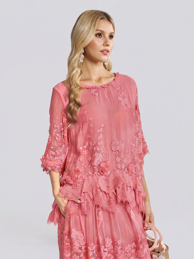 A person with long blonde hair wears the Social Queen 3D Floral Embroidered 100% Silk Ruffle Blouse, featuring delicate floral embroidery and subtle ruffle detailing on the three-quarter sleeves, paired with a small bag and posing against a light grey background.
