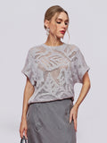 A woman wears the Social Queen Cutout Jacquard Knit Top in light gray, featuring short sleeves and a delicate botanical floral pattern, paired with a gray skirt and posing against a plain background.