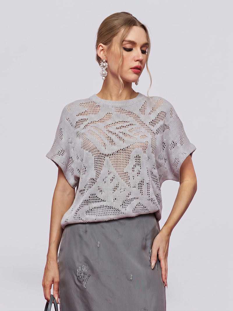 A woman wears the Social Queen Cutout Jacquard Knit Top in light gray, featuring short sleeves and a delicate botanical floral pattern, paired with a gray skirt and posing against a plain background.