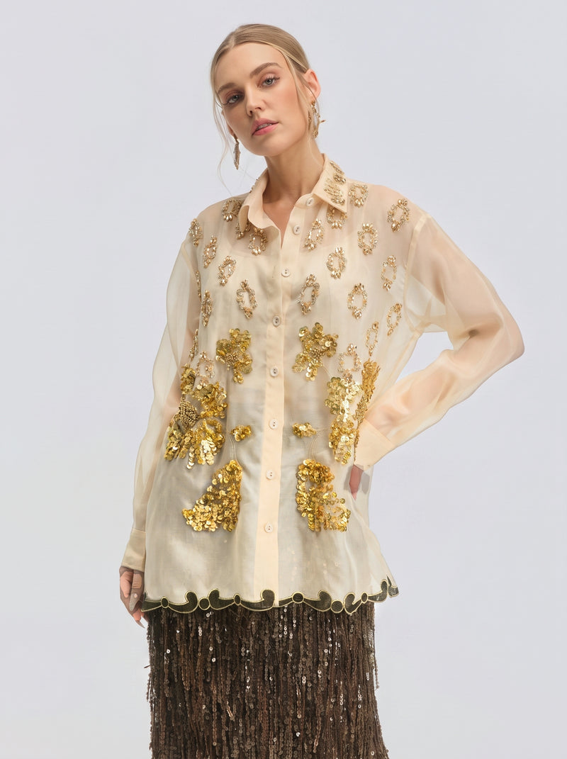 A woman models the Social Queen Floral Sequin Mulberry Silk Shirt, featuring a beaded collar and gold sequin embellishments, styled with a brown fringed skirt against a plain background.