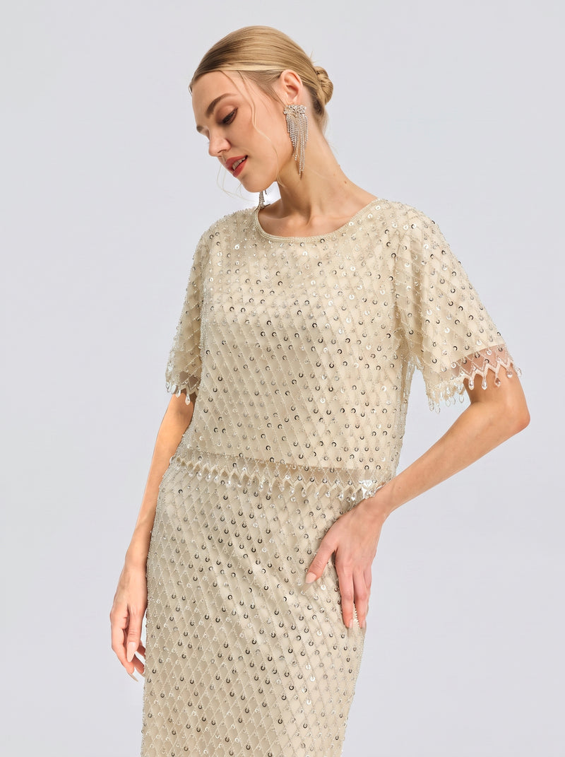A woman wears the Social Queen Crystal Beaded Fringe Top, styled for a chic occasion with her hair in a low bun and head gently tilted downward against a plain light background.