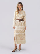 A woman models the Social Queen Embroidered Fringe Lace Crystal-Trimmed Dress—a long cream gown featuring delicate hand-embroidered openwork, lace details, and fringe accents—cinched at the waist with a wide brown belt and styled with a statement necklace and strappy heels against a plain light background.