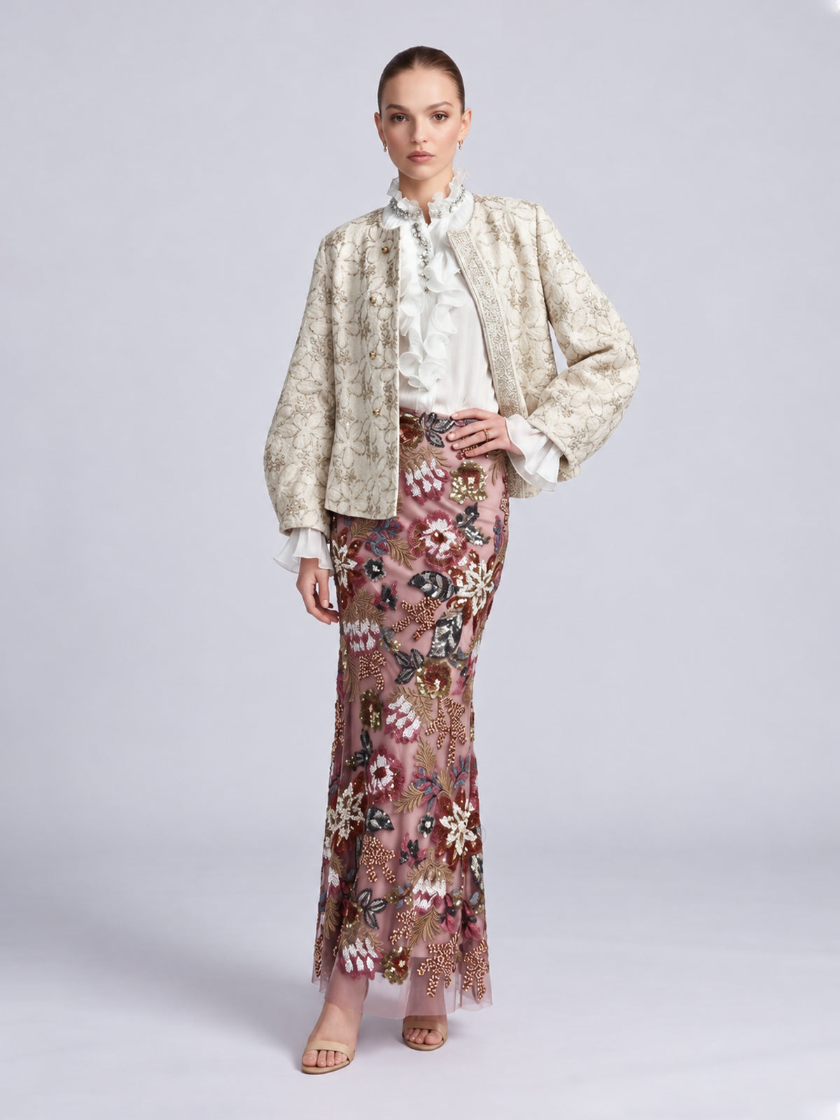 A model wears a light-colored Floral Appliqué Embroidered Jacket by Social Queen over a white ruffled blouse and a floor-length pink skirt with floral embroidery and beadwork.